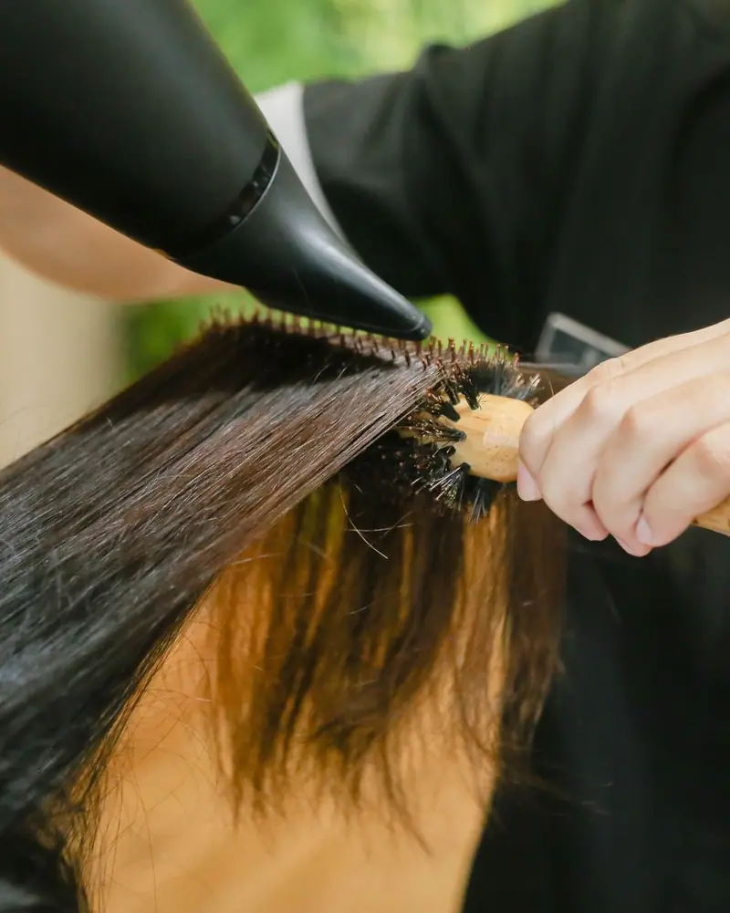 Stylist blow-drying long dark hair with a round brush