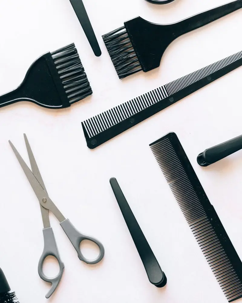 Hairdressing brushes, combs and scissors laid out on a white surface